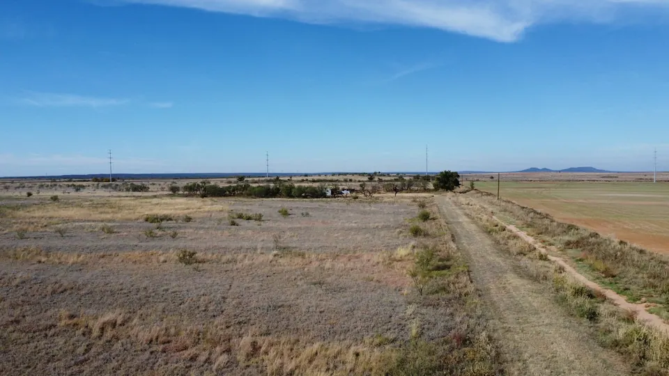 Expansive Texas ranch land with native grasses, cultivated fields, and distant hills under a clear sky on 240 acres in Fisher County