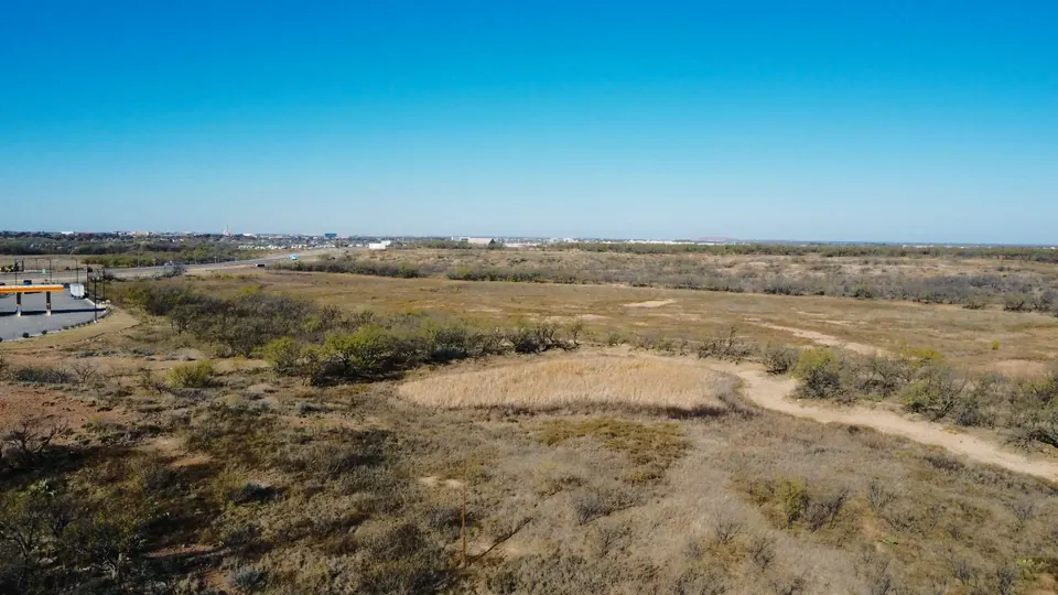 Expansive acreage in Taylor County with native grasses, scrub brush, and distant city views