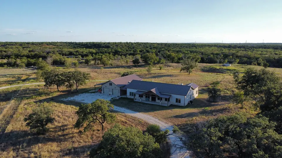 Ranch house with metal roof and attached garage sits amid native grasses and trees on 320 acres in Taylor County