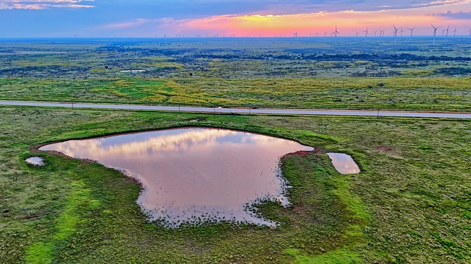 Stock pond reflecting the sky on a Texas ranch with distant wind turbines on 430 acres in Archer County